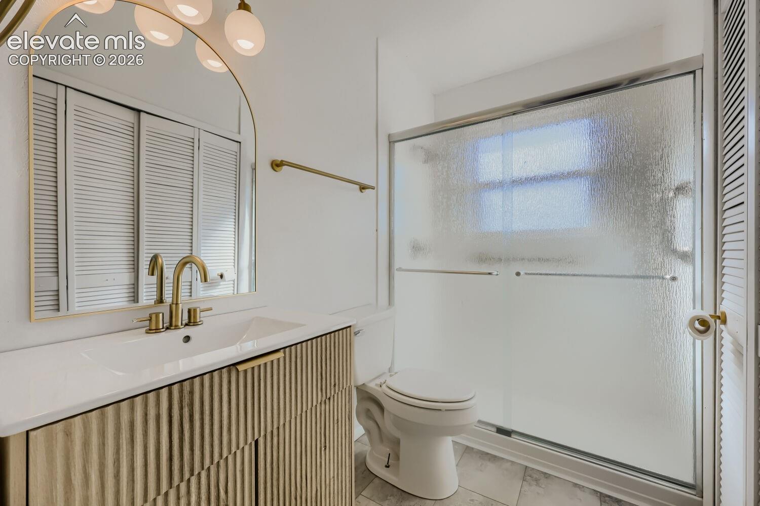 Spa-inspired primary bathroom featuring a floating vanity with brass hardware, white quartz countertop, and an arched brass-framed mirror with integrated lighting