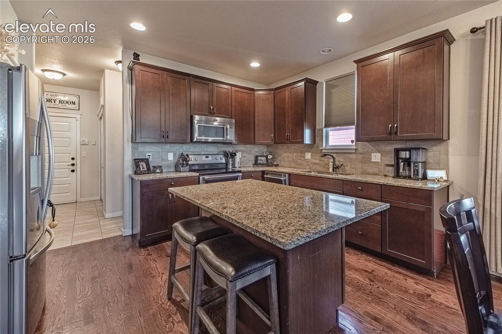 Kitchen featuring wood-finish cabinetry, stone-surfaced countertops, a center island with seating space, stainless steel appliances, and wood-finish flooring