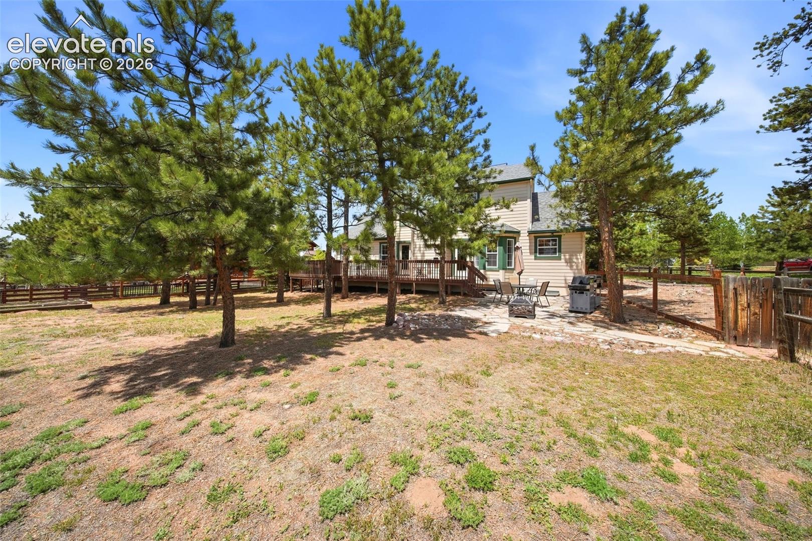 Expansive outdoor space featuring a two-story residence with light-colored siding and dark green trim, a multi-level wood deck, and a flagstone patio