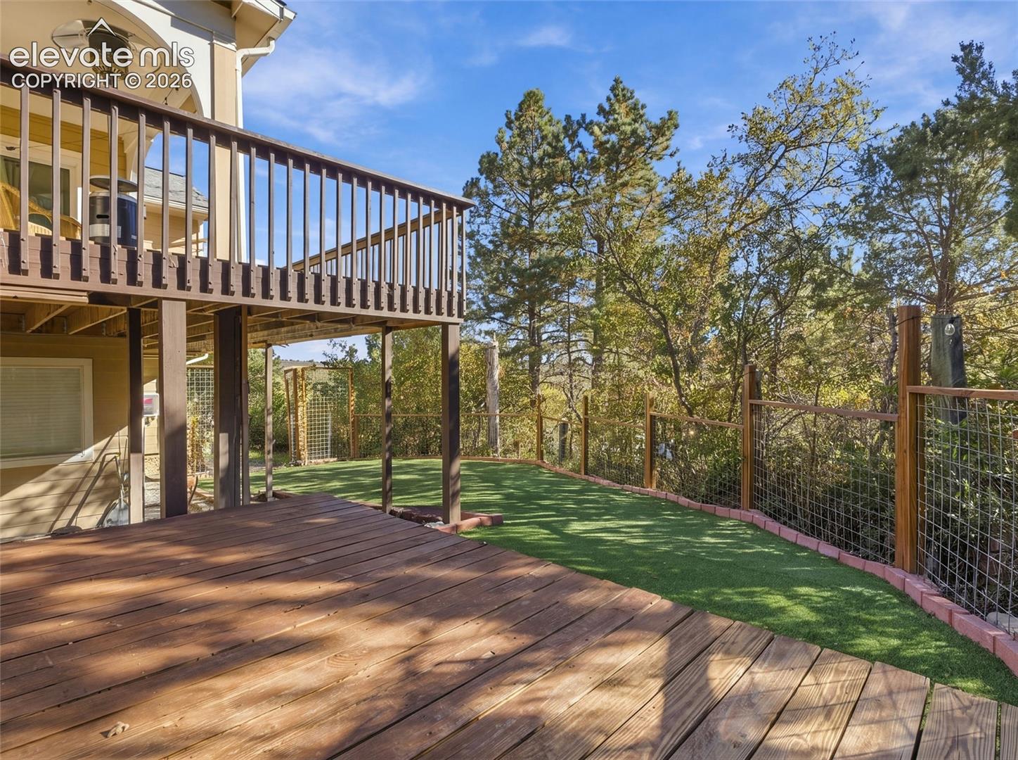 Multi-level wooden deck featuring vertical balusters, synthetic turf lawn, and perimeter wood and wire fencing