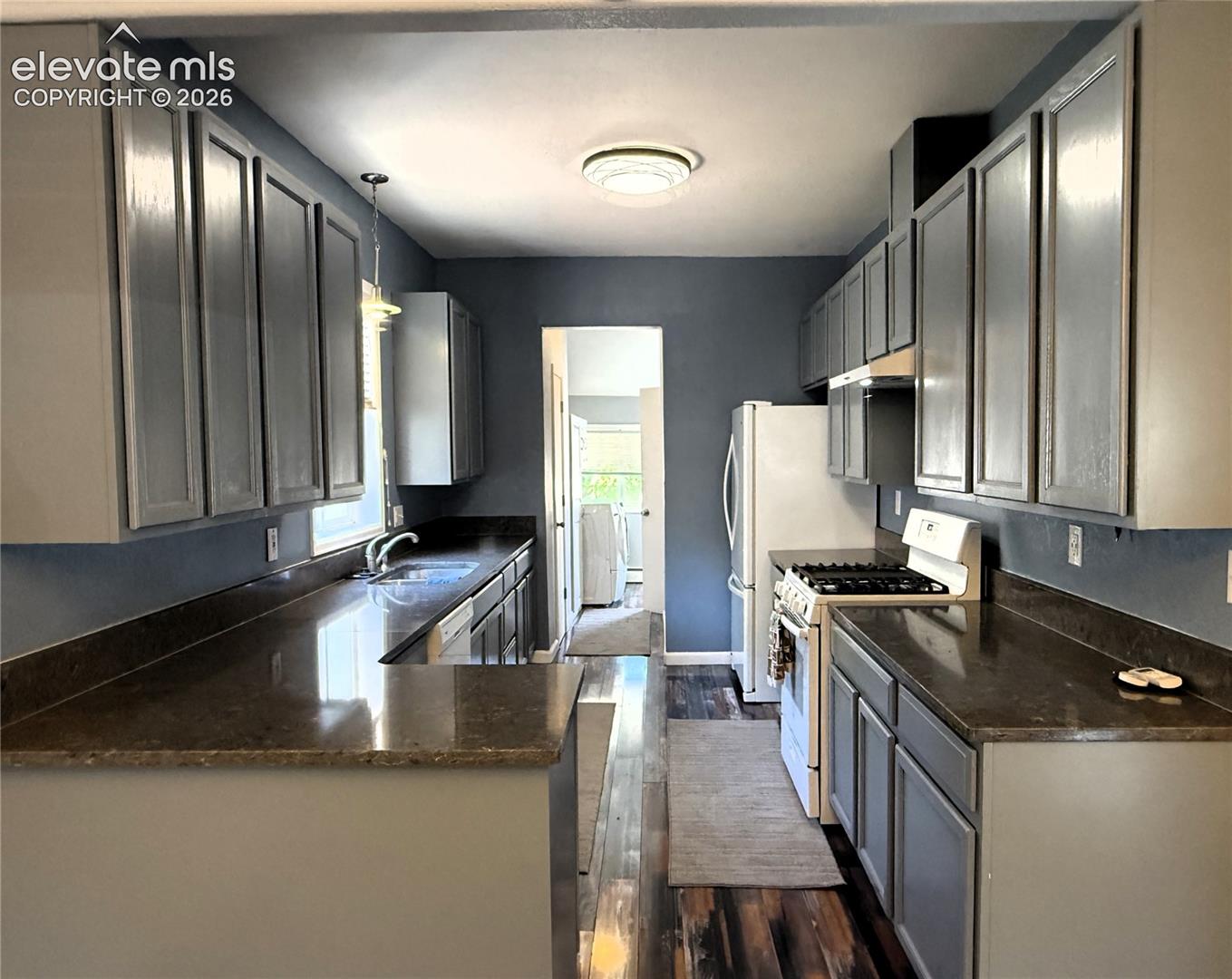 Kitchen featuring solid-surface countertops, dual-toned cabinetry, wood-finish flooring, and a stainless steel undermount sink