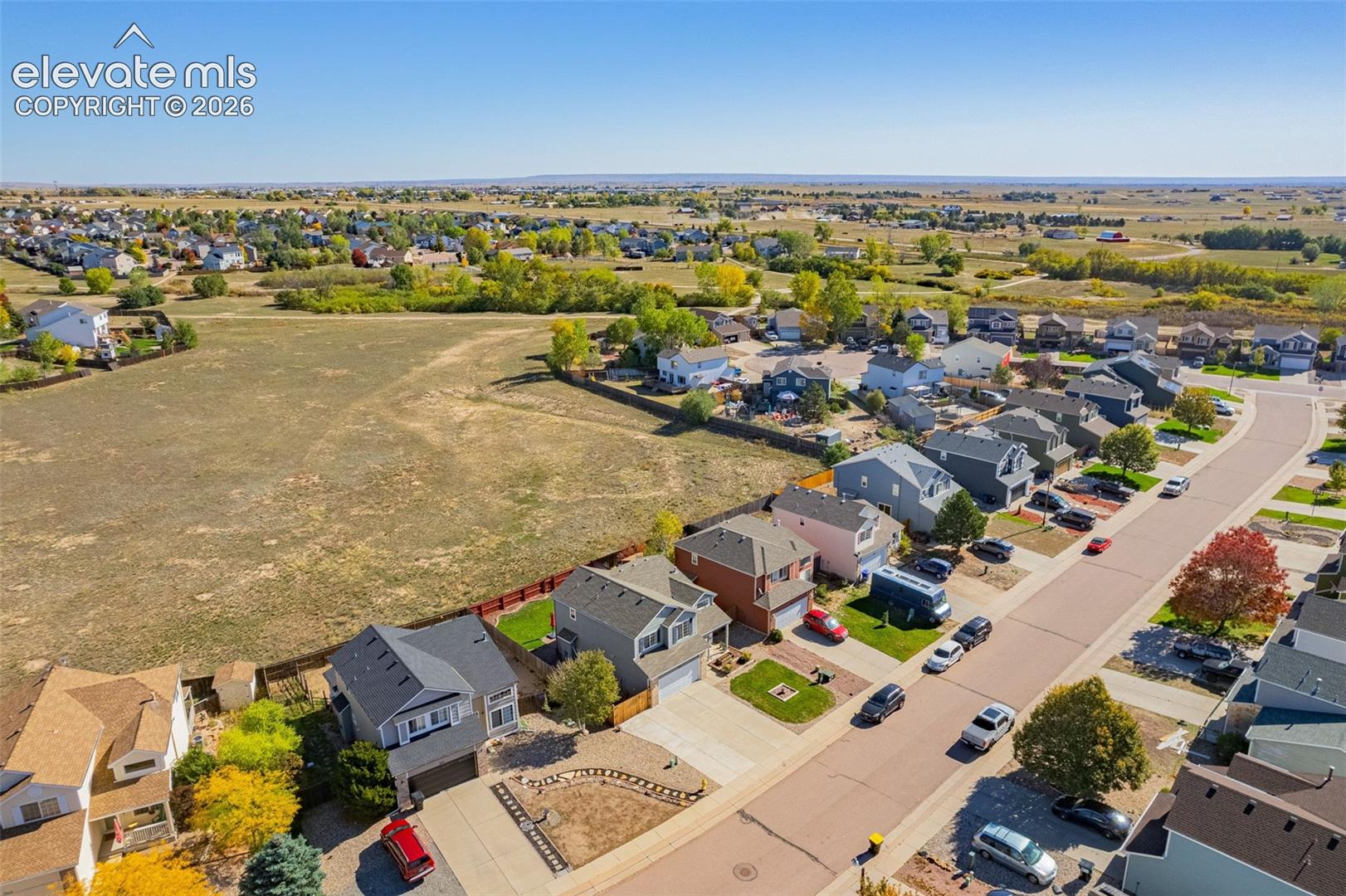 Aerial perspective of a suburban neighborhood featuring paved streets, multi-level residential structures with pitched roofing, concrete driveways, and expansive undeveloped open space