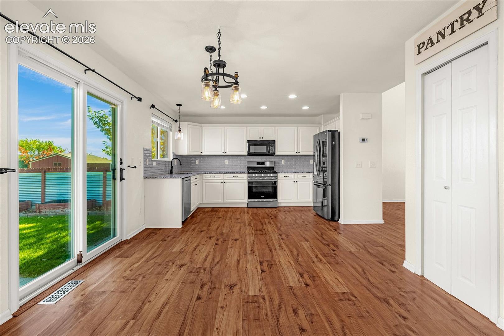 Kitchen featuring wood-finish flooring, white cabinetry, integrated stainless steel appliances, a tile backsplash, and sliding glass doors