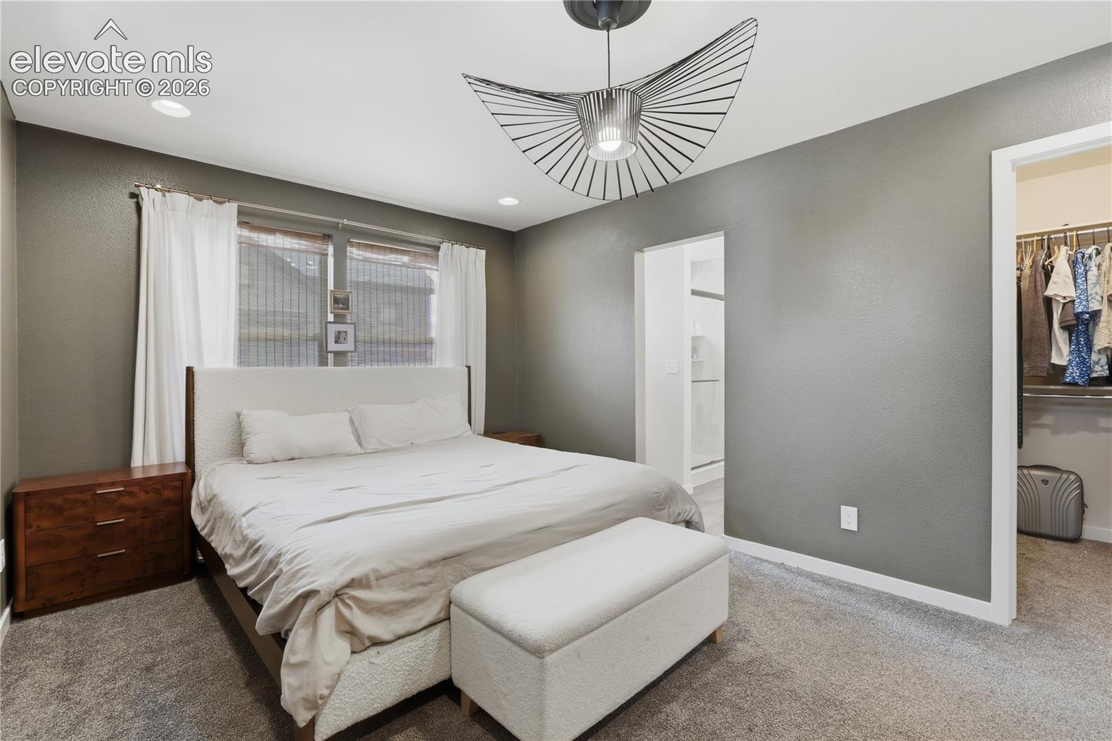 Carpeted bedroom with a window featuring white curtains and horizontal blinds