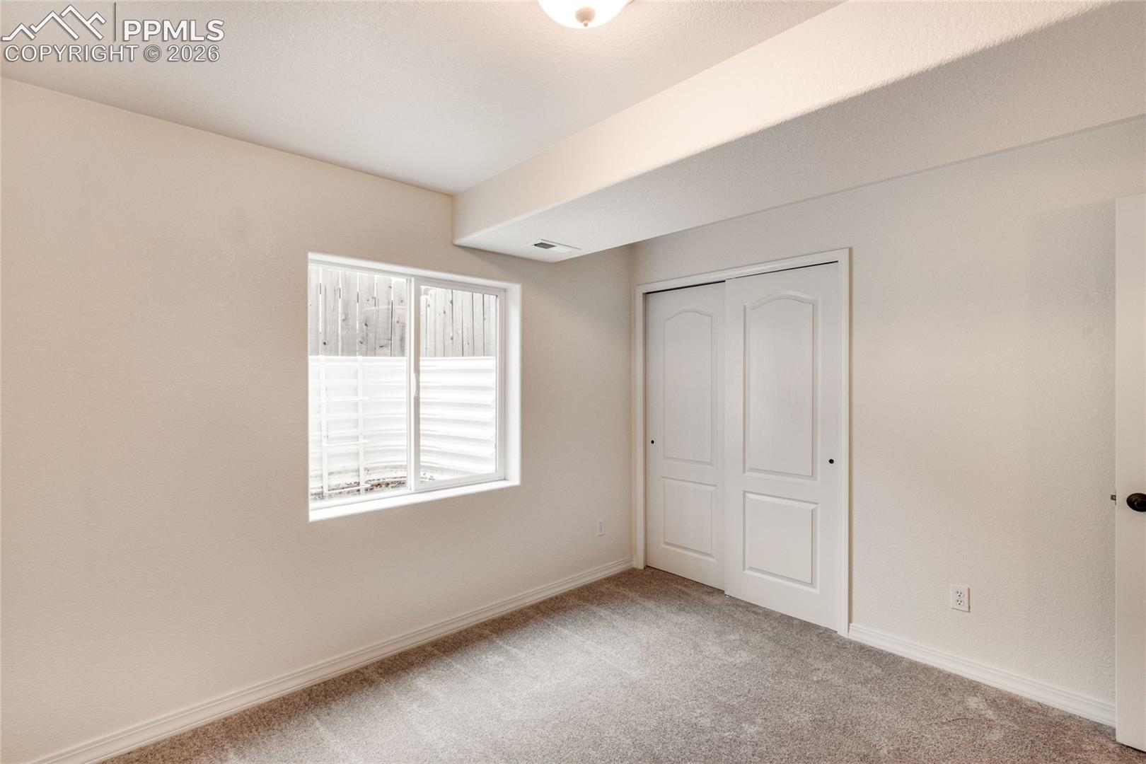 First basement bedroom with window and closet with sliding doors.