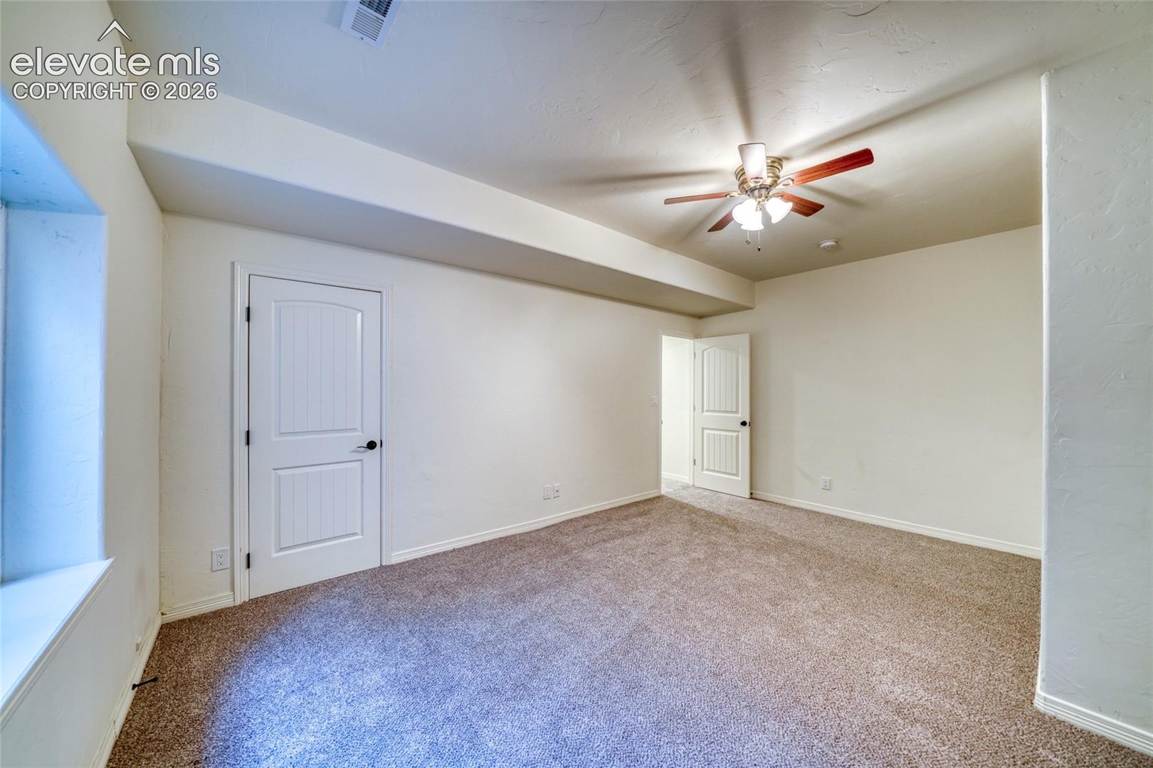 Spacious carpeted room featuring a ceiling fan, white paneled doors, and a window with a deep sill
