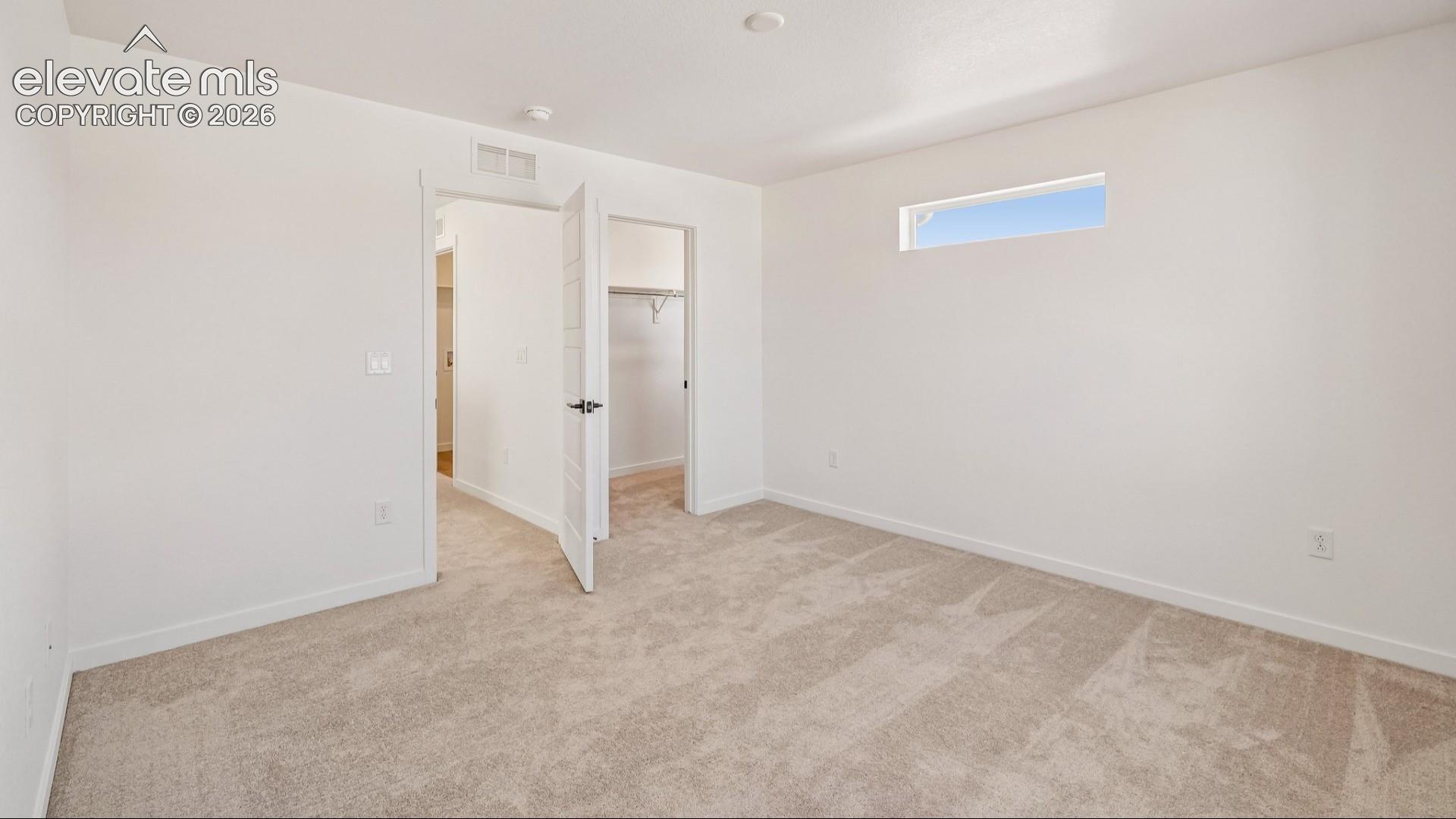 Neutral wall-to-wall carpeting, high-position rectangular window, multi-panel interior door, and walk-in closet