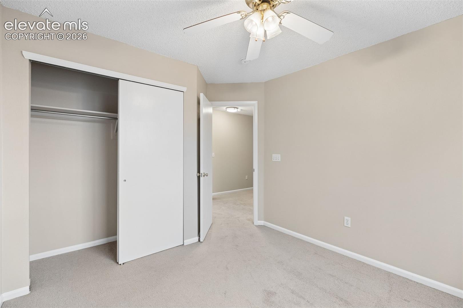 Neutral-toned interior featuring wall-to-wall carpeting, a sliding-door closet with overhead shelving, and a ceiling fan with integrated lighting