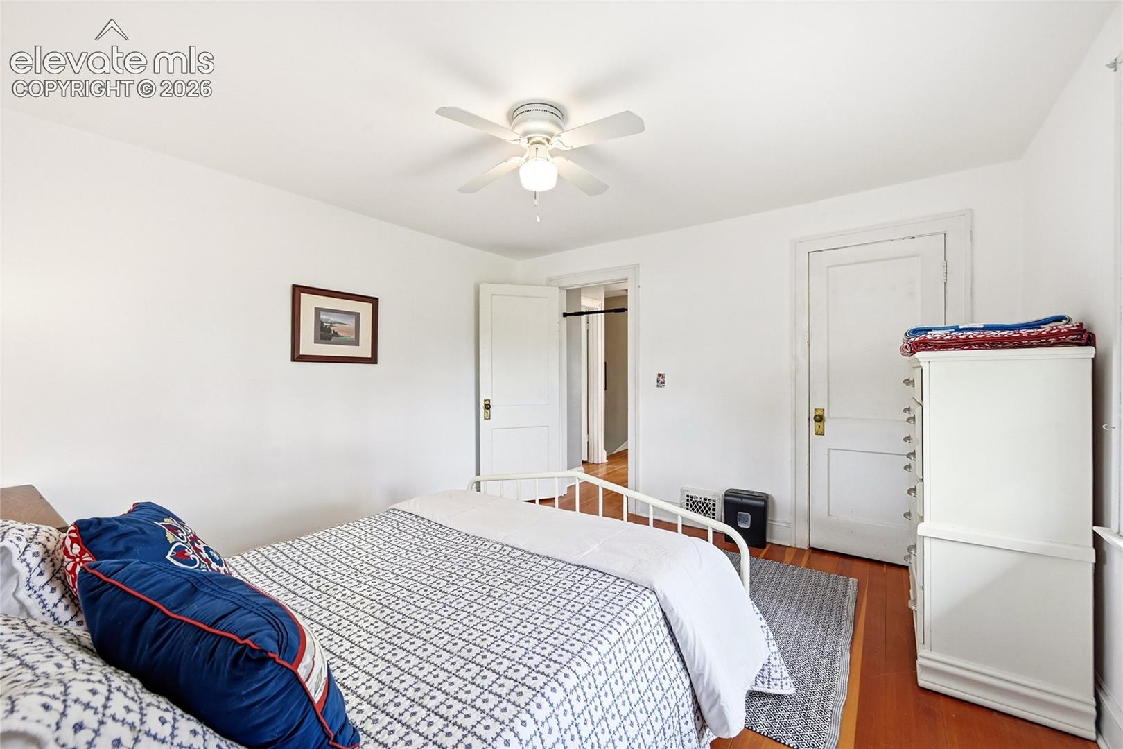 Bedroom featuring wood-finish flooring, a white ceiling fan with integrated lighting, and two solid-core interior doors with traditional hardware