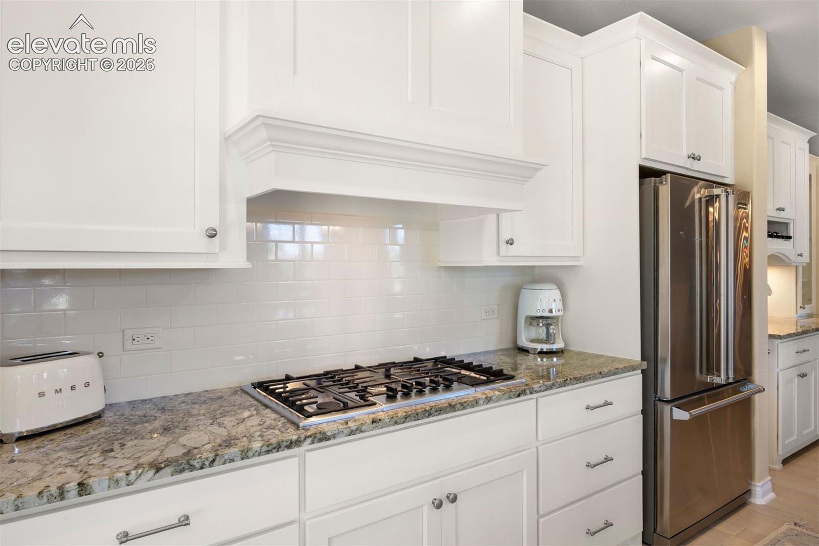 Kitchen featuring white cabinetry, granite countertops, a gas cooktop, a subway tile backsplash, and a stainless steel refrigerator