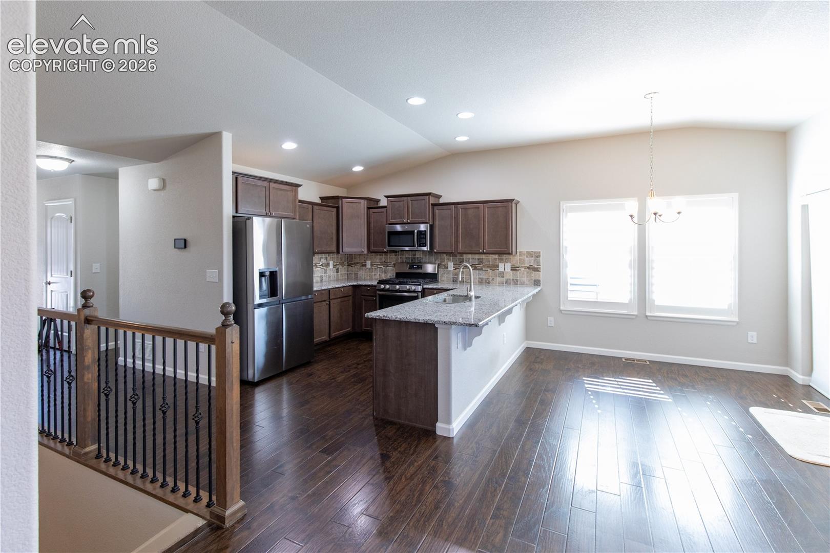Kitchen featuring dark-toned cabinetry, a stone-surfaced kitchen island, stainless steel refrigerator, recessed lighting, and wood-finish flooring