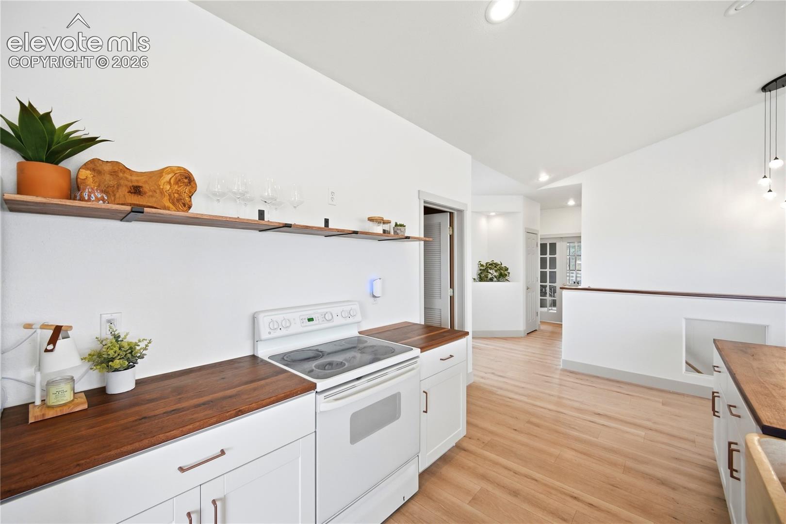Kitchen featuring white cabinetry, wood-finish countertops, floating shelving, vaulted ceilings, and wood-finish flooring