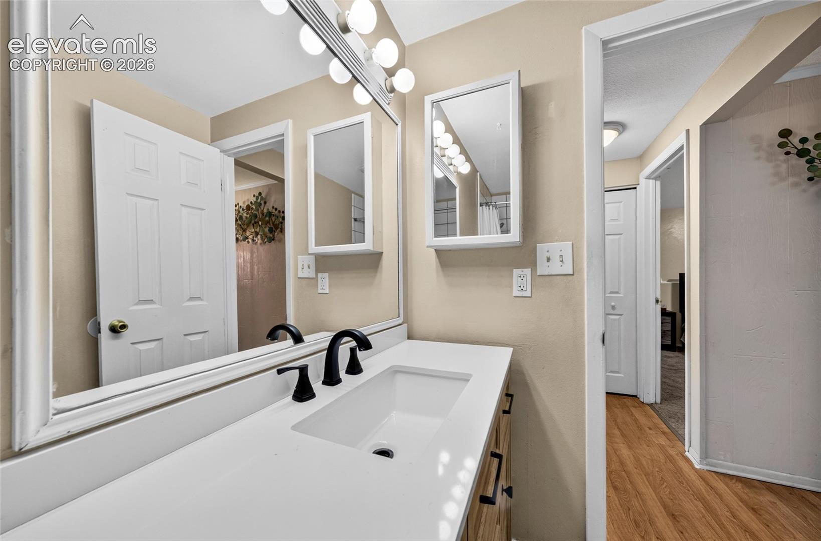 Vanity featuring a white countertop, integrated rectangular sink, matte black faucet, full-width mirror, and wall-mounted medicine cabinet with integrated lighting