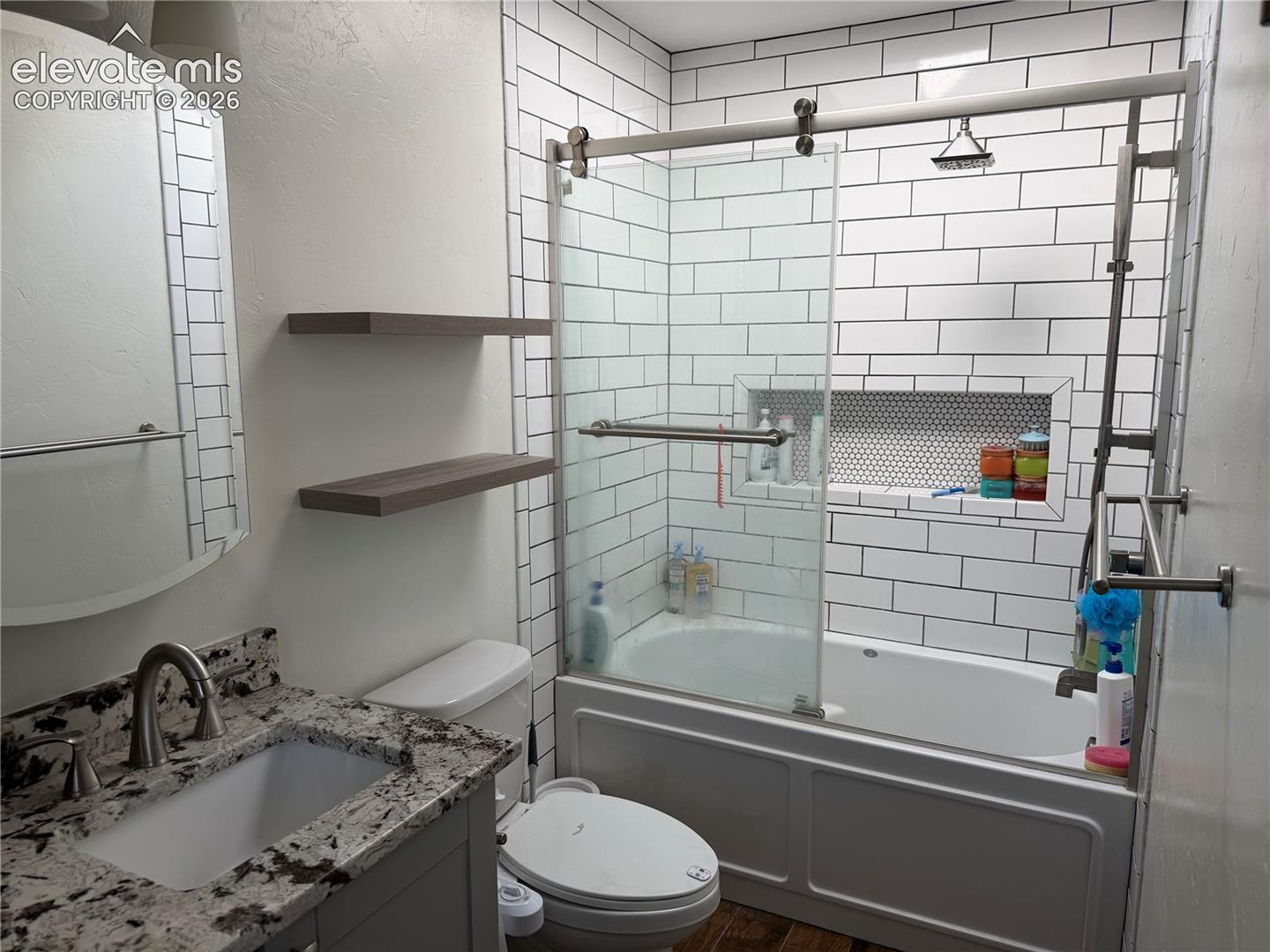 Bathroom featuring a subway tile shower surround, sliding glass shower door, recessed shower niche with penny tile, and a vanity with a stone countertop