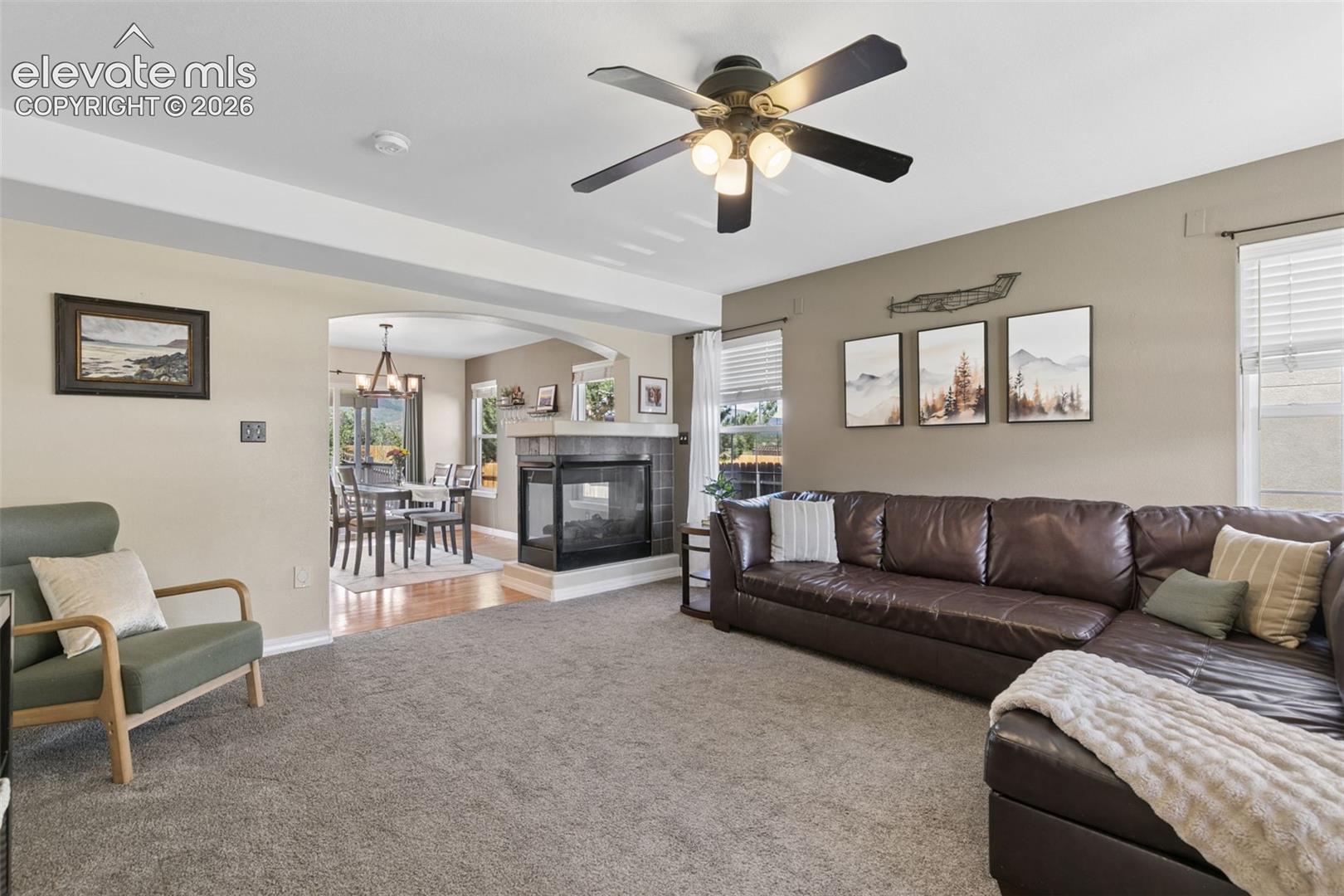 Carpeted living area with a ceiling fan, a tiled fireplace, and a dining room with wood-finish flooring