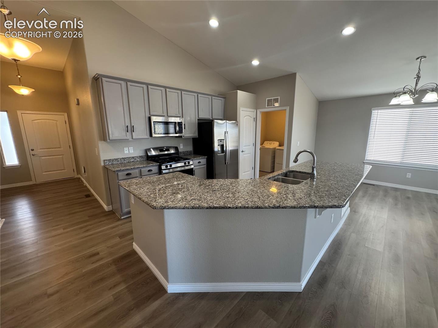 Kitchen featuring a peninsula island, stone-finish countertops, stainless steel appliances, shaker-style cabinetry, and wood-finish flooring