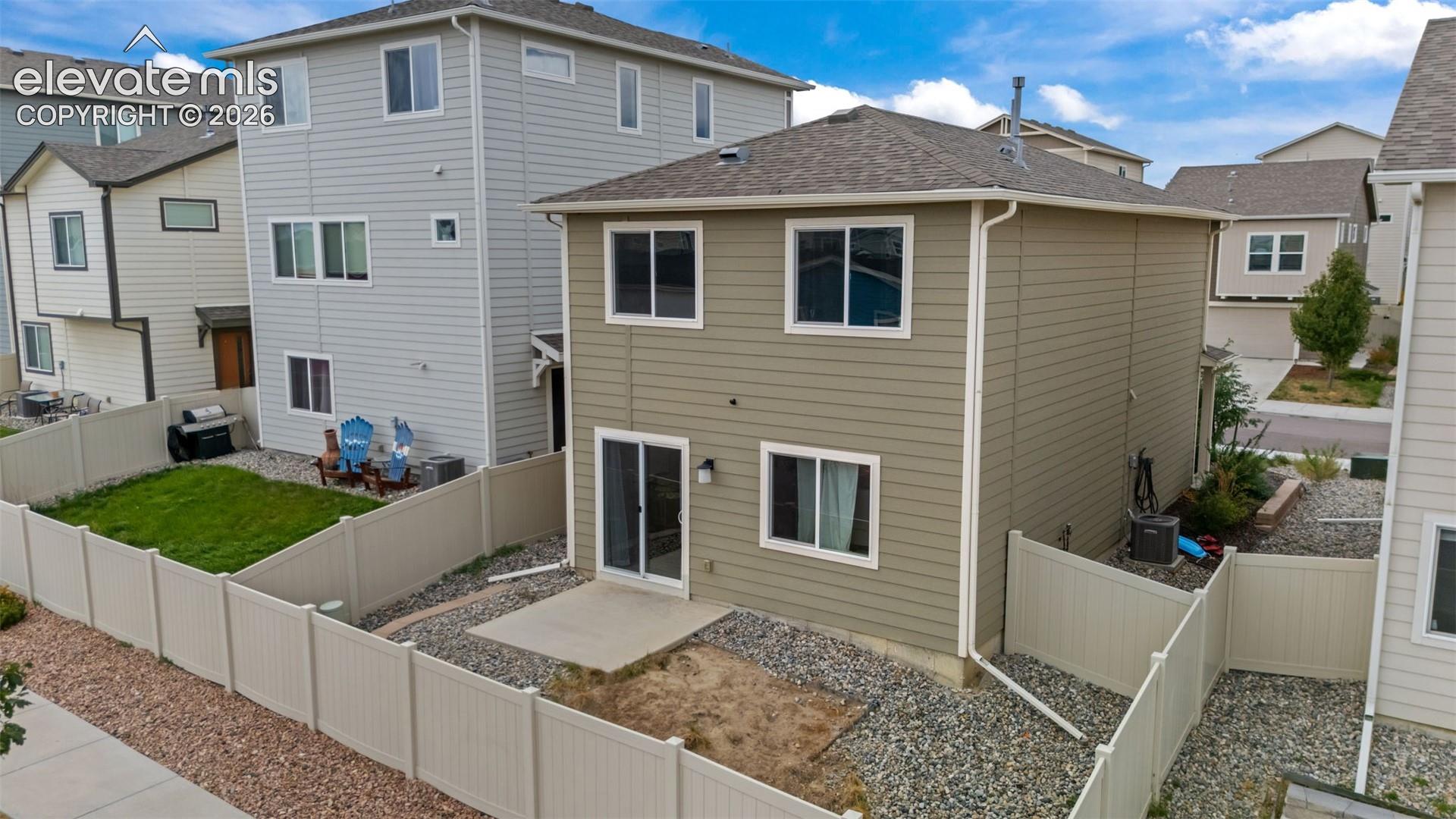 Rear exterior featuring horizontal siding, multiple windows, a sliding glass door, a concrete patio, and a fenced yard