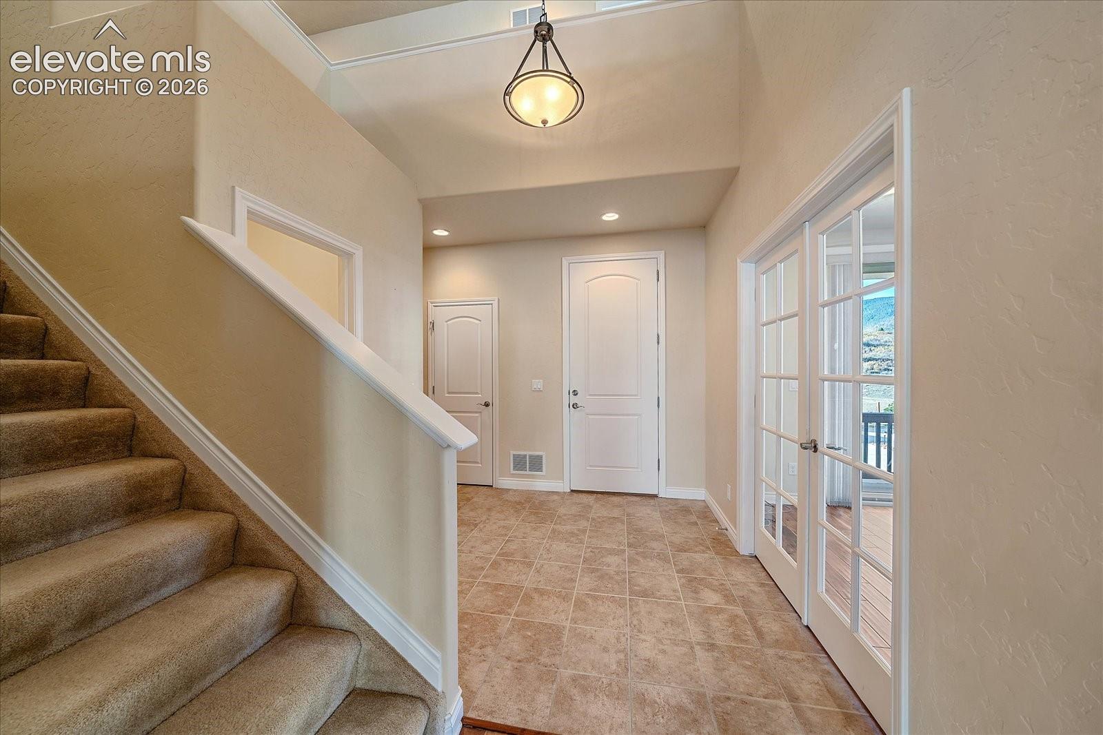 Foyer featuring high ceilings, neutral wall tones, tile flooring, a multi-light pendant fixture, and glass-paned French doors