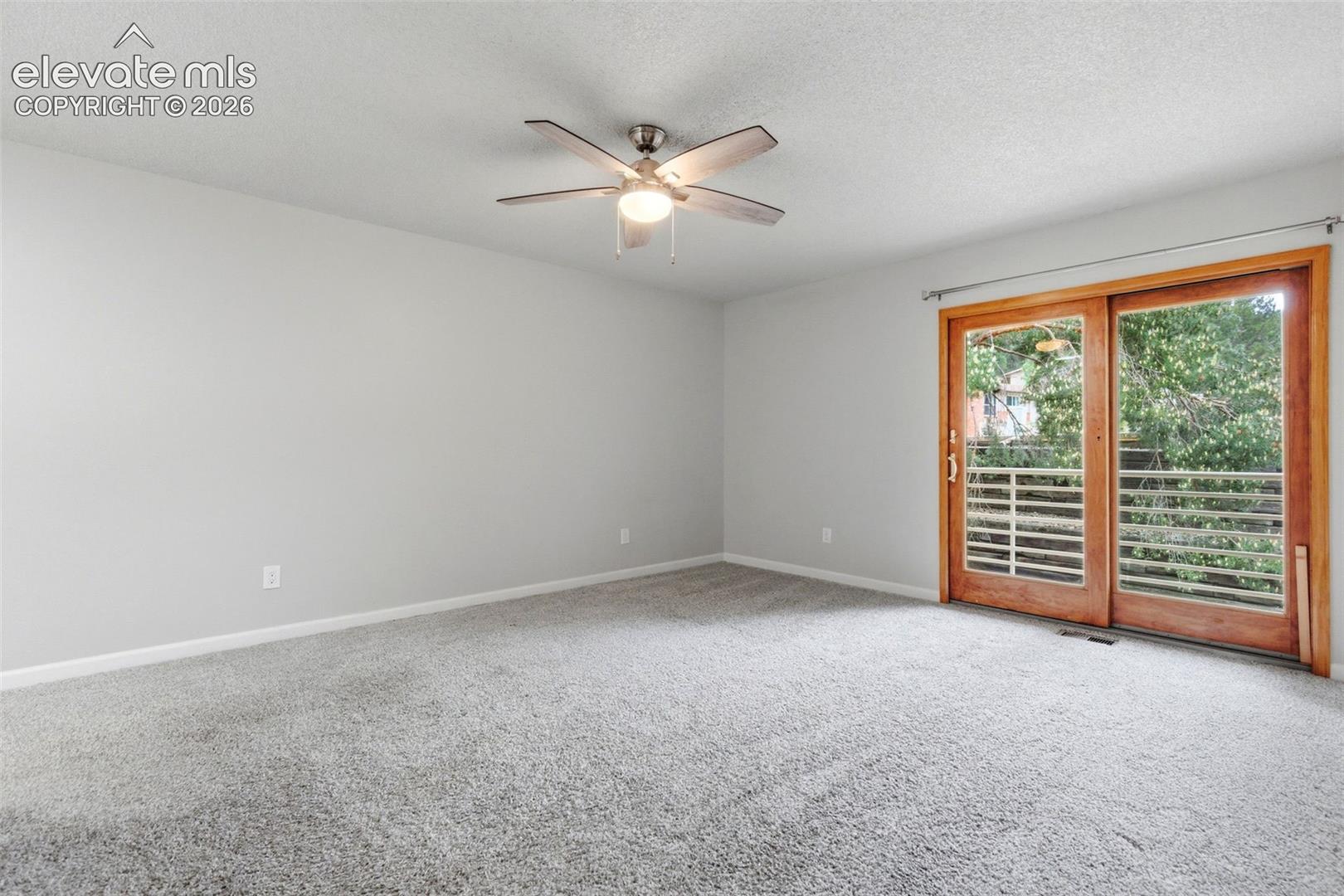 Spacious primary suite featuring light gray walls, plush gray carpeting, and a modern ceiling fan with integrated lighting