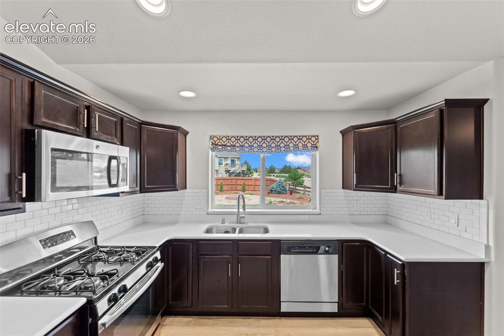 U-shaped kitchen with dark wood cabinetry, stainless steel appliances, white subway tile backsplash, and light-toned countertops