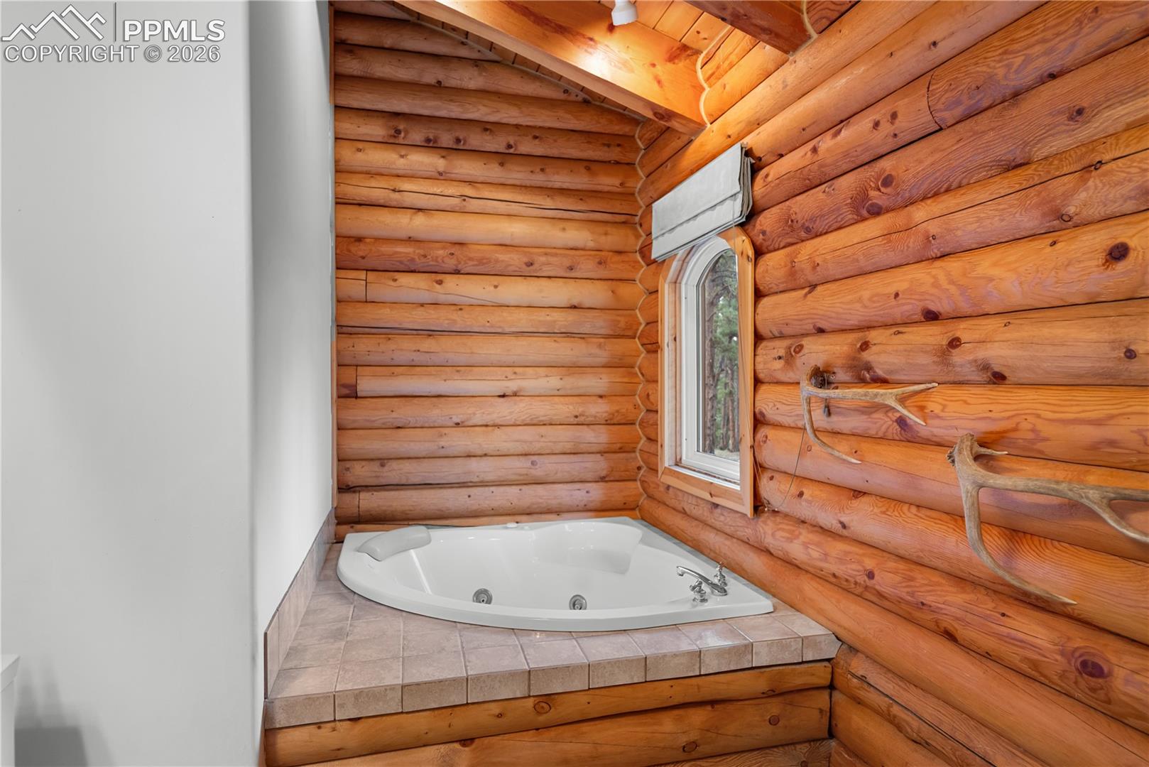 Full bath featuring a jetted tub, log walls, and beam ceiling