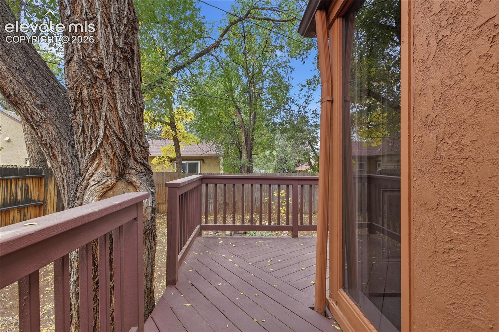 Outdoor wood deck featuring a painted balustrade, wood-frame glass slider, and mature trees