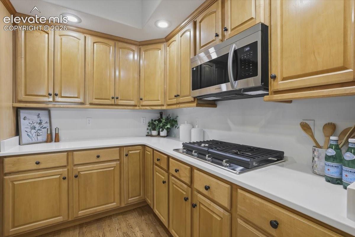 Wood-finish cabinetry with black hardware, white countertops, built-in stainless steel microwave, and integrated cooktop