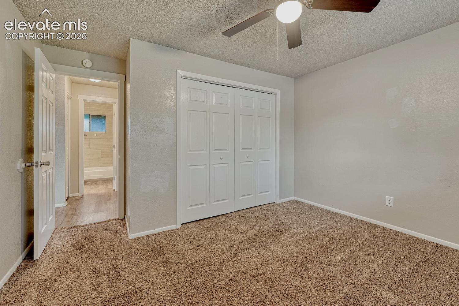 Brown carpet flooring, white bi-fold closet doors, ceiling fan with integrated lighting, textured ceiling