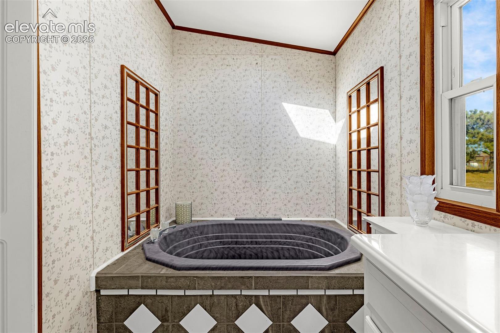 Built-in soaking tub with a tiled surround, diamond-patterned accent inlay, dual wood-framed wall mirrors, and a single-hung window