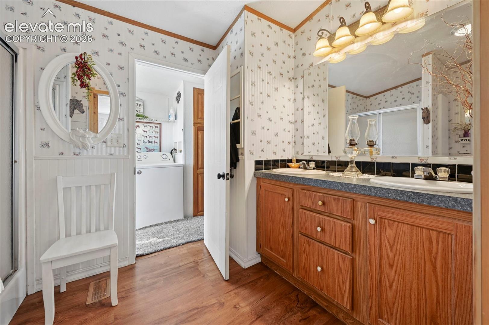 Double vanity with wood-finish cabinetry, solid-surface countertop, dual drop-in sinks, and a large-format mirror featuring a multi-bulb light fixture