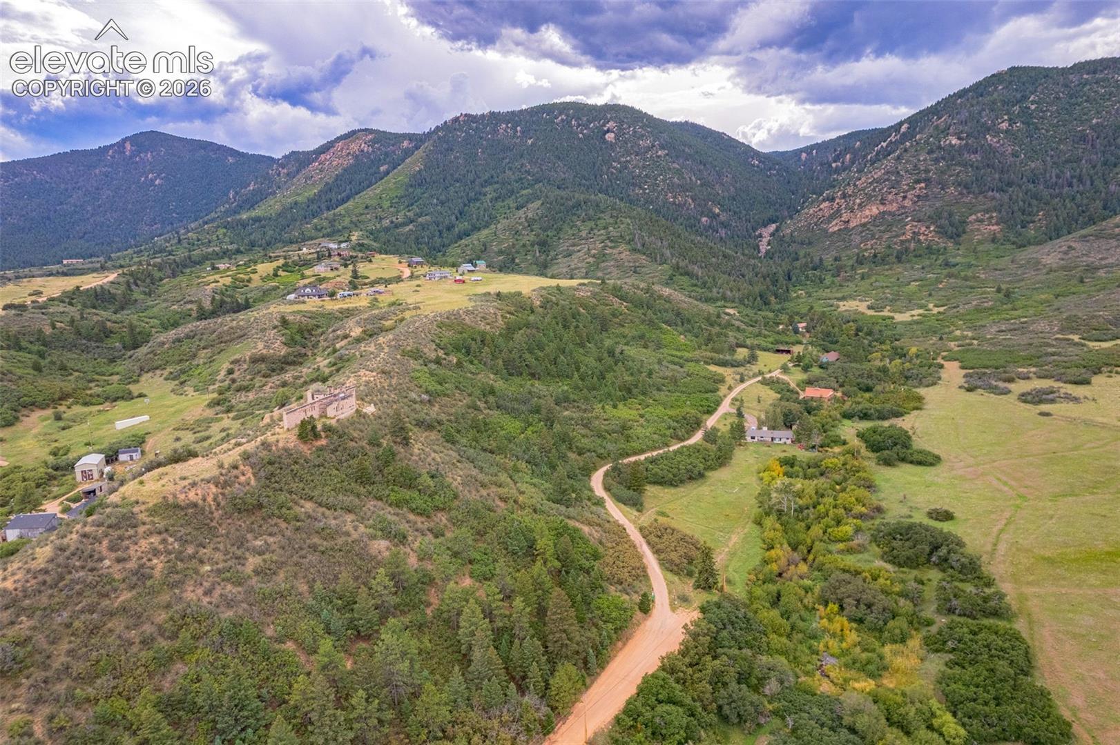 Mountainous terrain with natural landscaping, a winding dirt road, and multiple residential structures