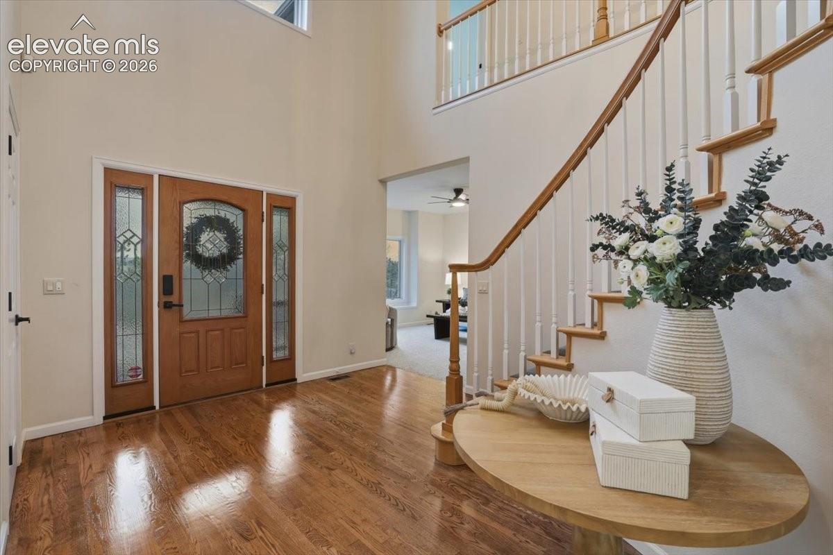 Hardwood flooring with a decorative wood entry door and sidelights, featuring a prominent staircase with wood banister and white spindles