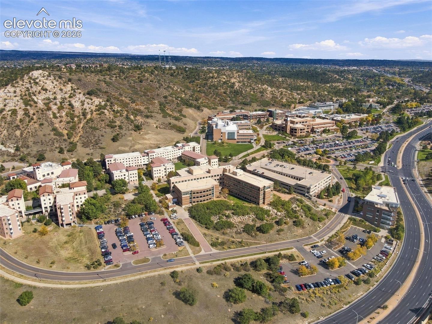 Aerial perspective featuring multi-story commercial buildings, paved surface parking lots, paved access roadways, and surrounding natural rock formations