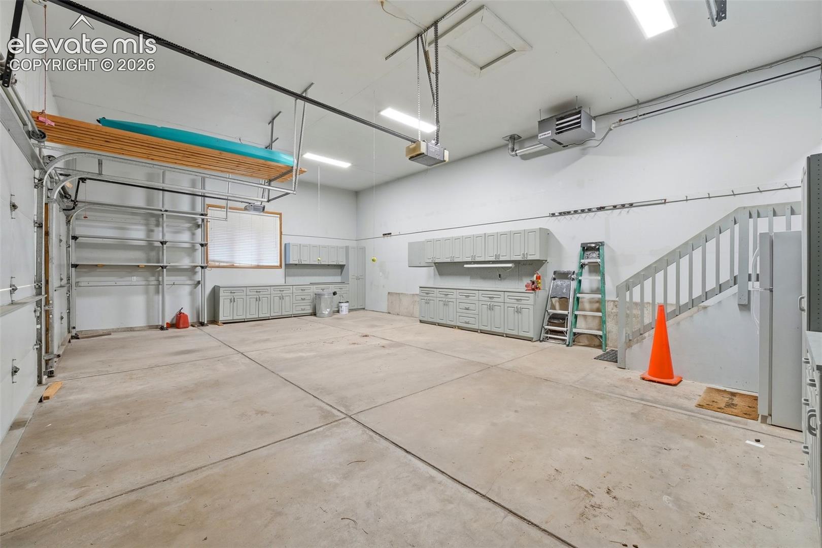 Concrete flooring garage featuring extensive cabinetry, overhead storage, integrated lighting, and a utility staircase