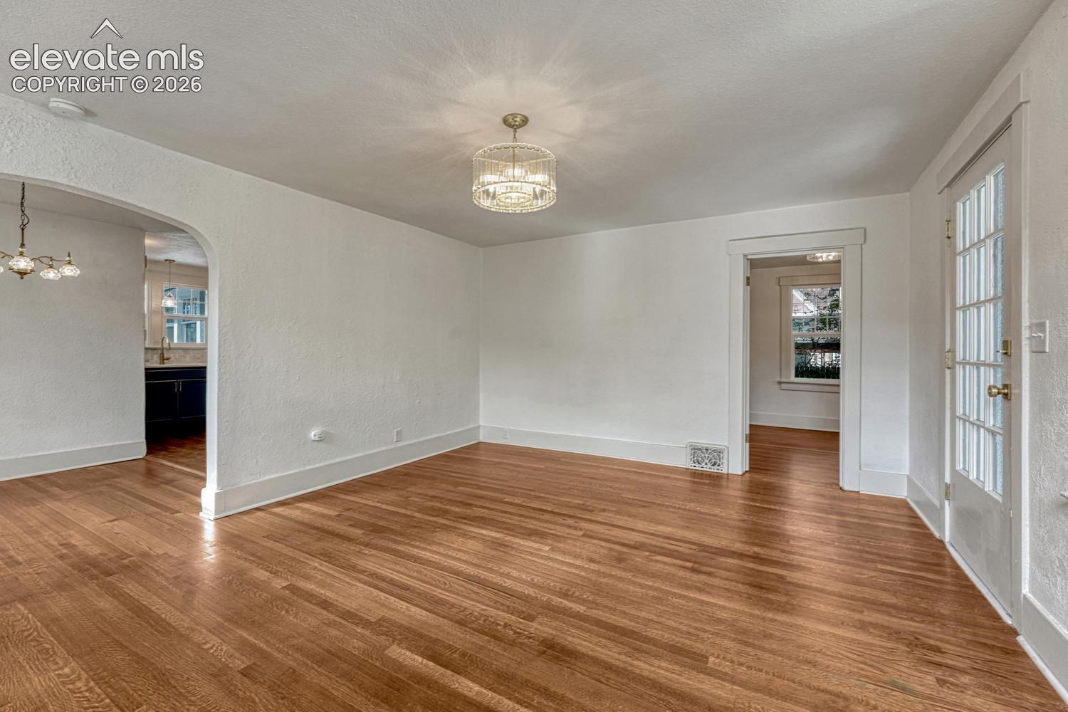 Hardwood flooring throughout, arched doorway, French door with multiple glass panes, contemporary ceiling light fixture, and white wall finishes