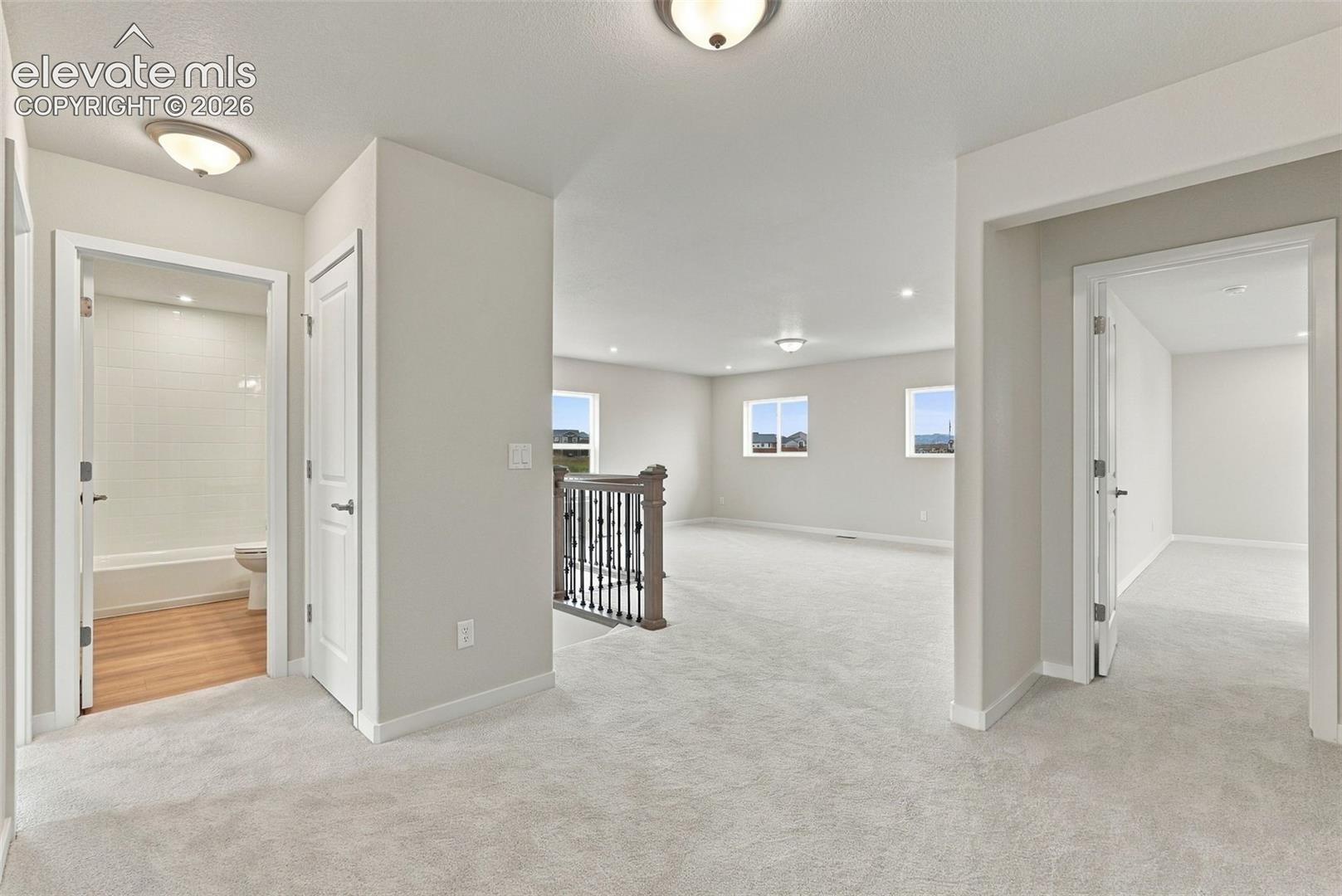 Neutral-toned wall-to-wall carpeting, open-concept floor plan, metal baluster staircase railing, and recessed ceiling lighting