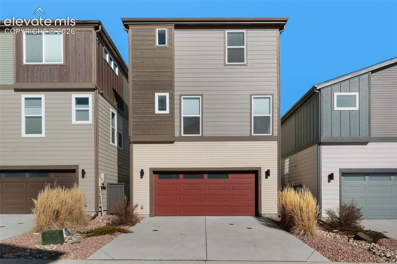 Three-story residence featuring a red garage door, concrete driveway, and multi-tone siding