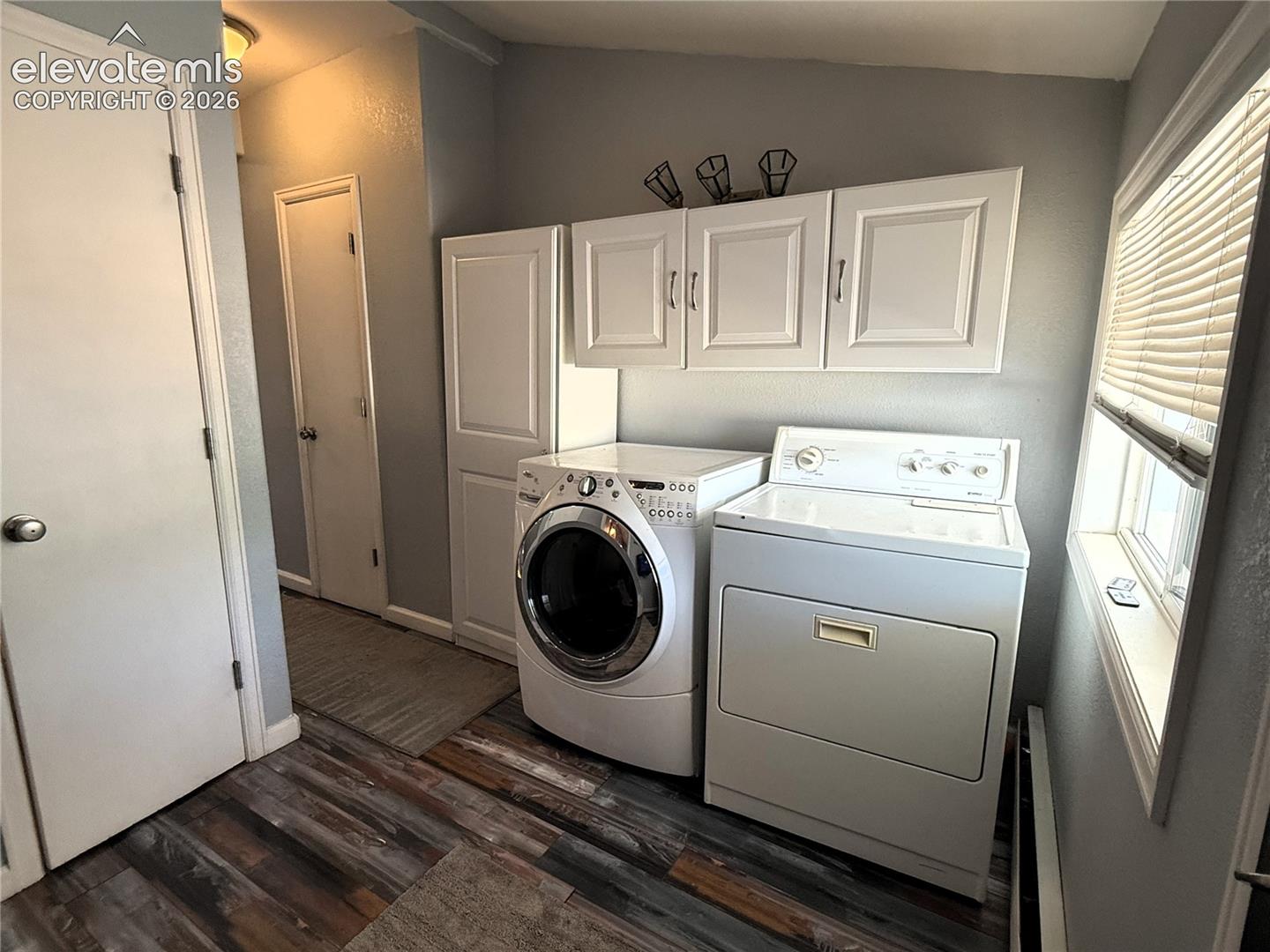 Utility space featuring wood-finish flooring, white shaker-style wall cabinets, a tall built-in storage pantry, and neutral wall tones
