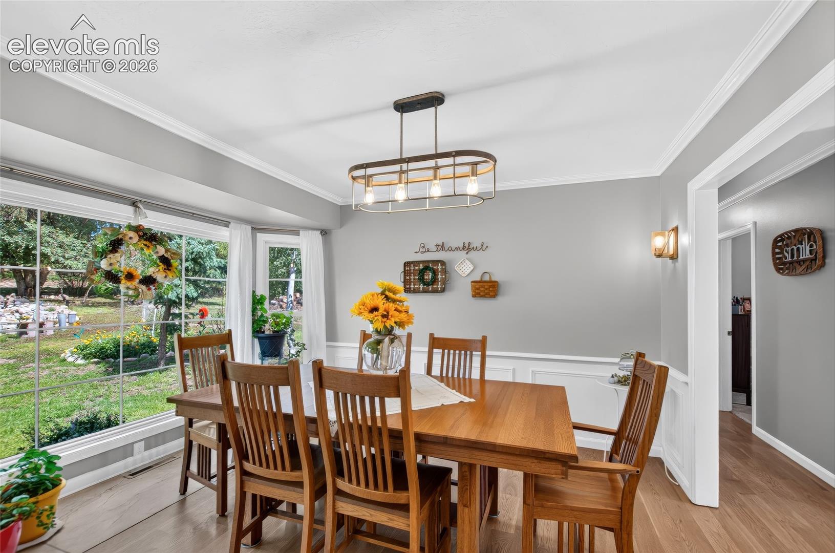 Bright dining space with a large bay window, crown molding, and wainscoting