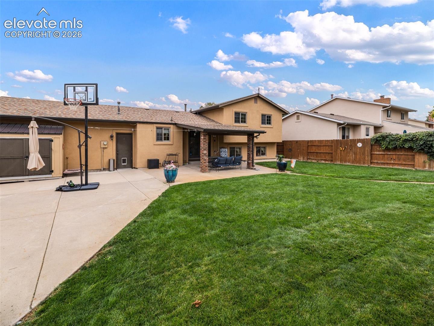 Expansive green lawn, concrete patio, covered outdoor living space, stucco exterior, and a wood privacy fence