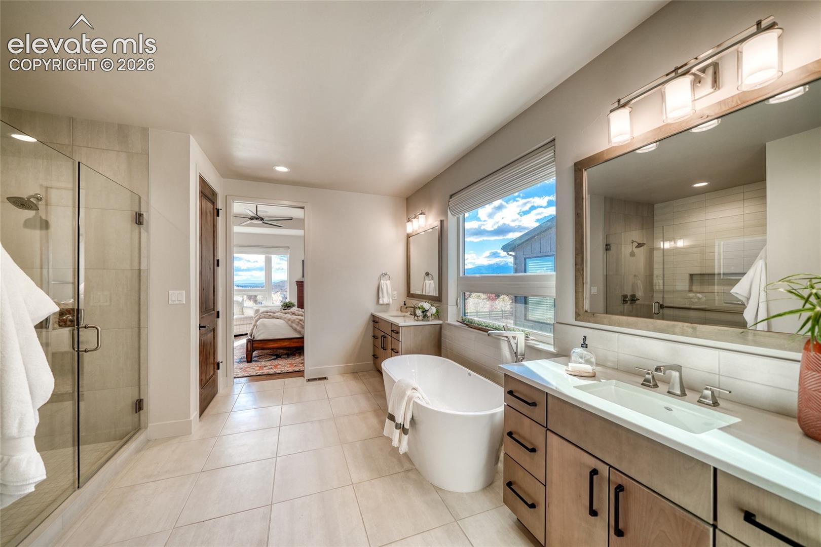 Freestanding soaking tub, walk-in tile shower with glass enclosure, dual-sink vanity with wood-finish cabinetry, rectangular under-mount sinks, and large-format tile flooring