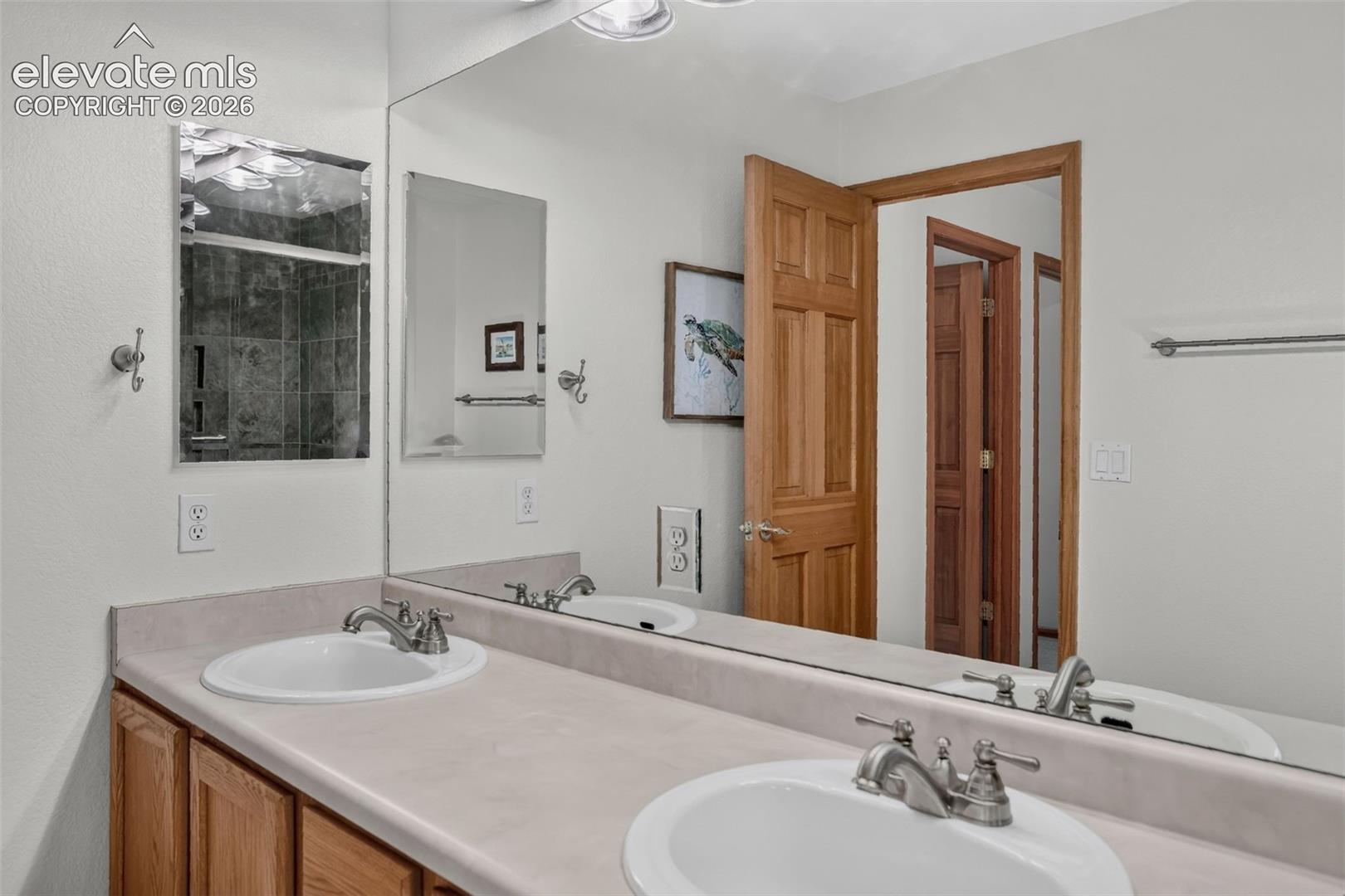 Bathroom featuring a dual-sink vanity with light-toned countertops, wood-finish cabinetry, and brushed nickel fixtures