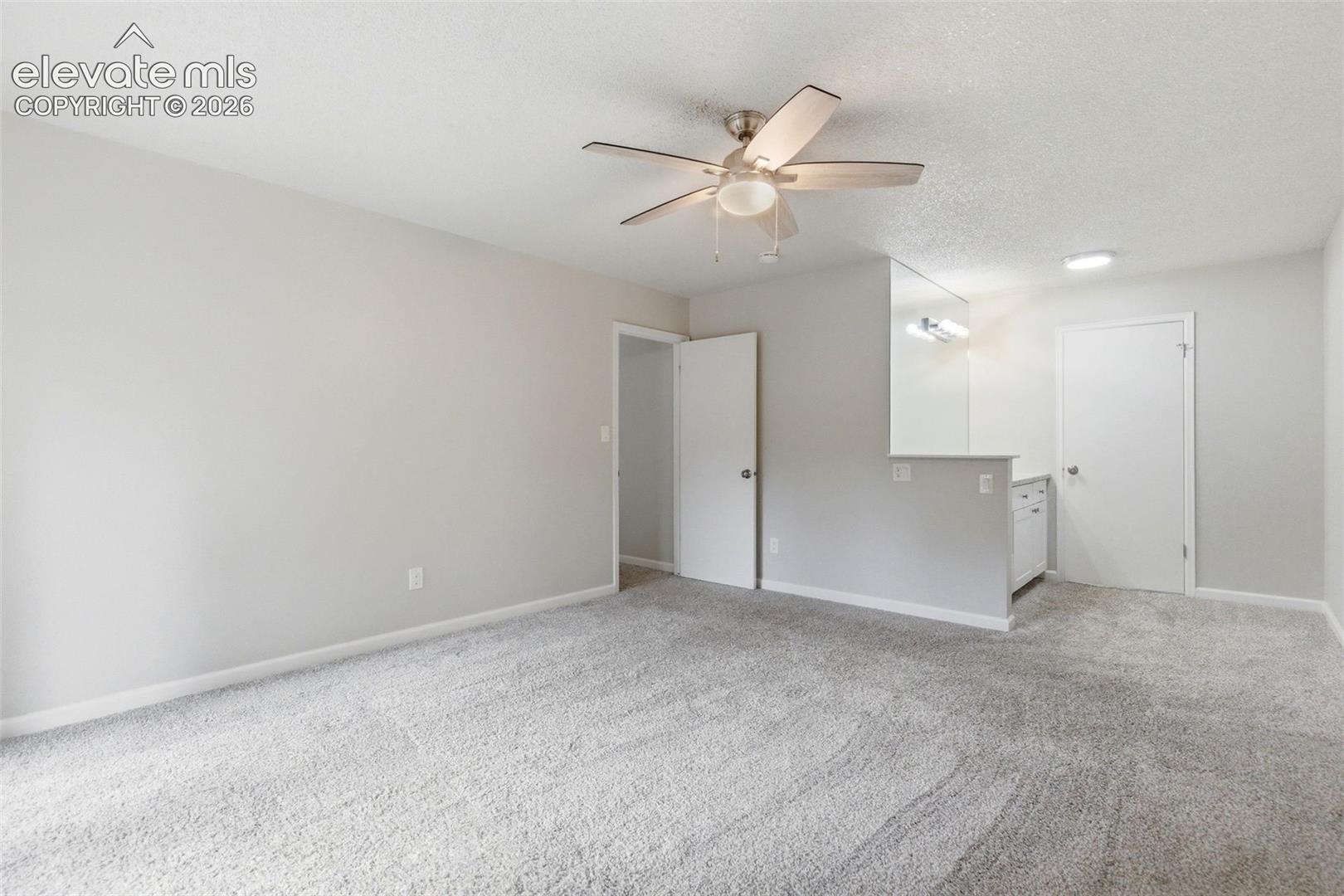 Spacious room featuring light gray walls, textured white ceilings, and neutral carpet flooring
