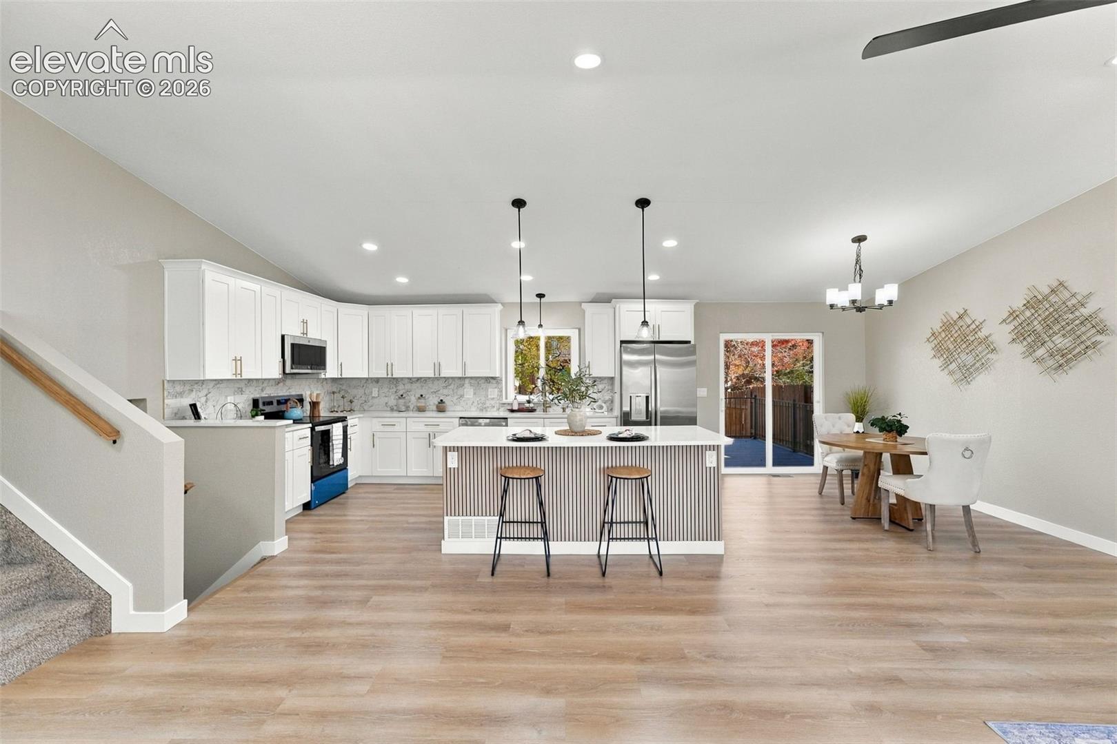 Kitchen featuring white shaker-style cabinetry, stainless steel appliances, a center island with vertical paneling, recessed lighting, and wood-finish flooring