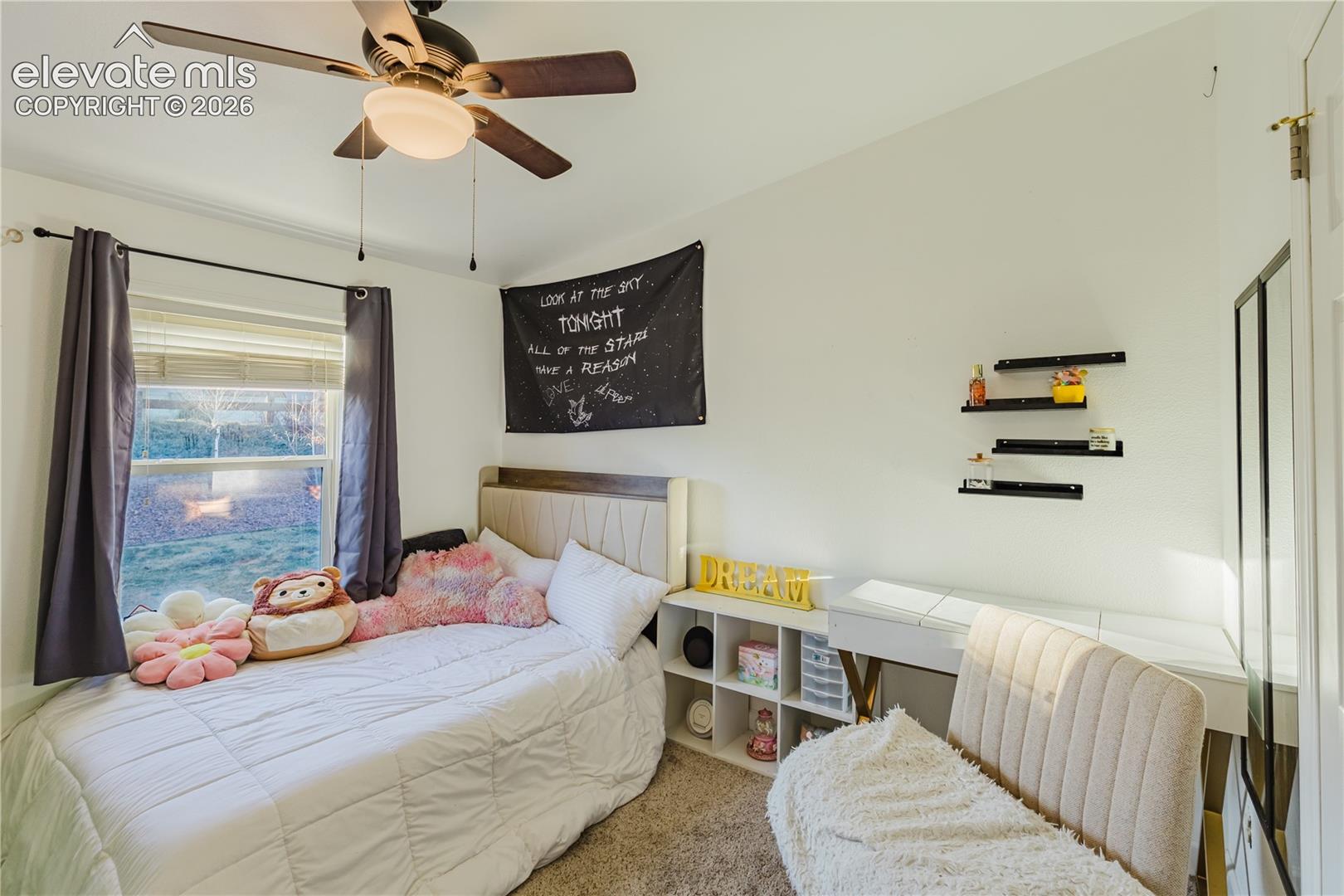Bright secondary bedroom featuring a ceiling fan with integrated lighting, built-in window seat with storage below, floating shelves for display, and carpeted flooring