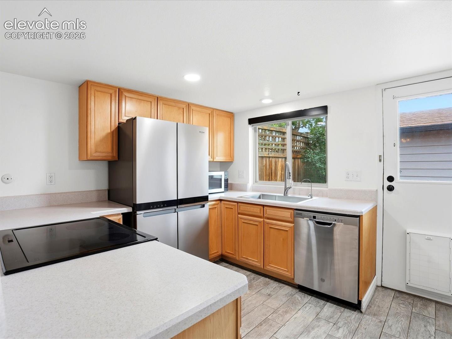 Kitchen featuring light wood cabinetry, stainless steel appliances, solid surface countertops, a stainless steel sink, and wood-finish tile flooring
