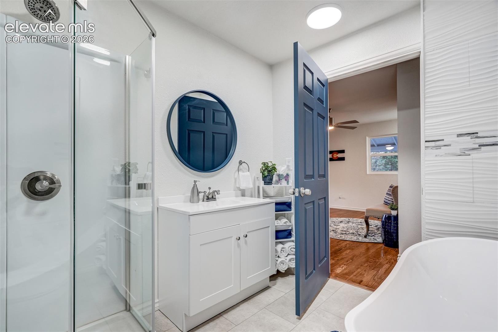 Walk-in shower with glass enclosure, single vanity with white cabinetry, round wall mirror, and wave-patterned accent wall