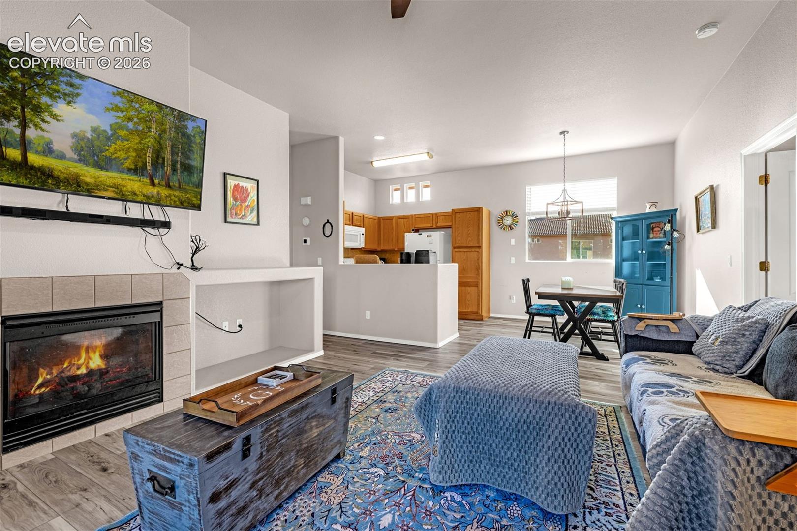 Living area featuring a fireplace with neutral tile surround, built-in recessed shelving, wood-finish flooring, and kitchen cabinetry