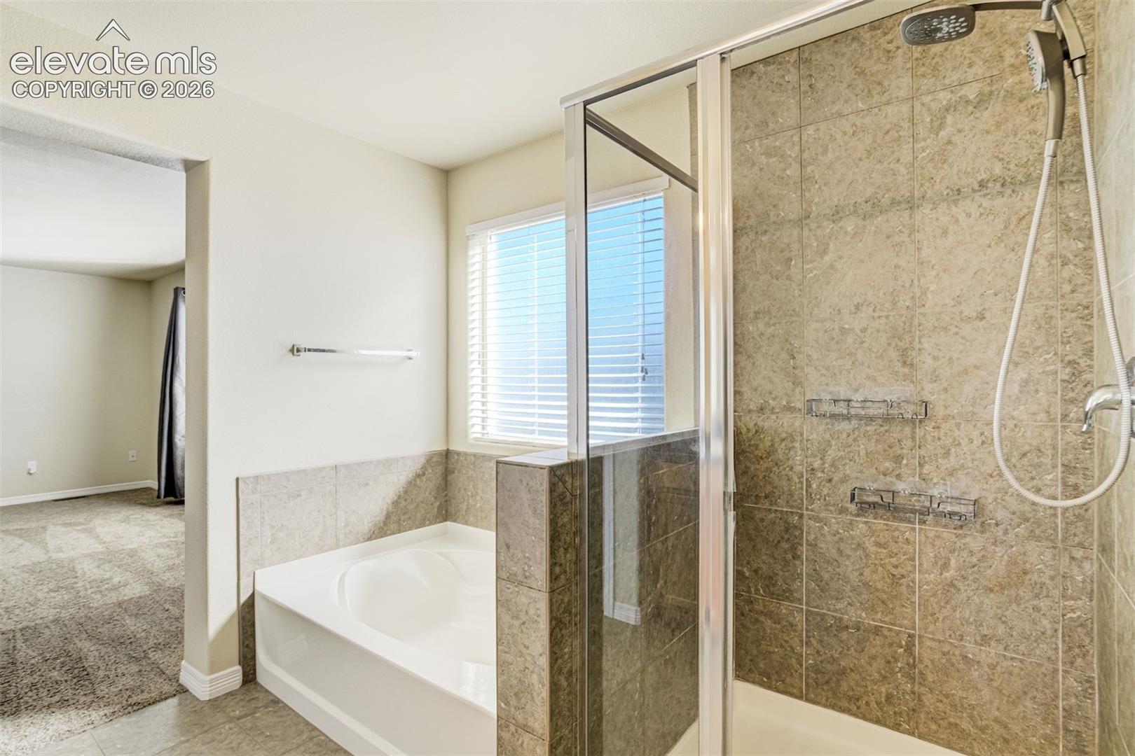 Glass-enclosed shower with a multi-function showerhead, tiled walls, and built-in shelving and a large soaking tub.