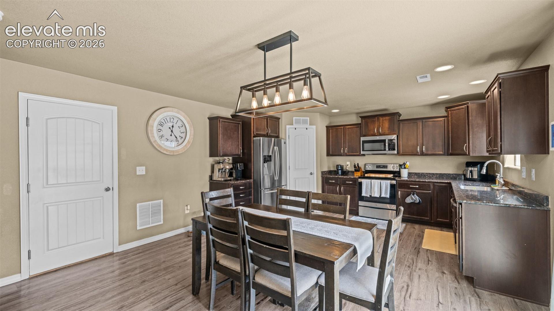 Open-concept kitchen and dining area featuring rich wood-finish cabinetry, dark countertops, and stainless steel appliances
